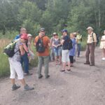 Rawa nieodkryta (wygumkowana) – czyli spacer z nieoczekiwanym zakończeniem grupka około 10 osób na ścieżce, w tle zarośla, a za nimi las