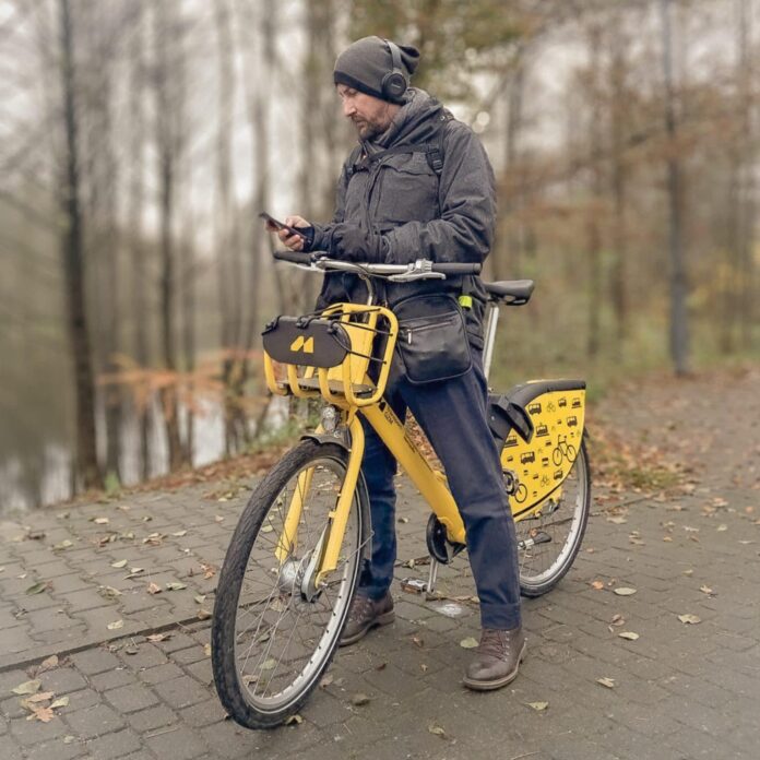 8f5b0b85-3484-4d53-ad25-812ad75d5dc2 Łukasz Folda stoi przy rowerze i przegląda telefon komórkowy
