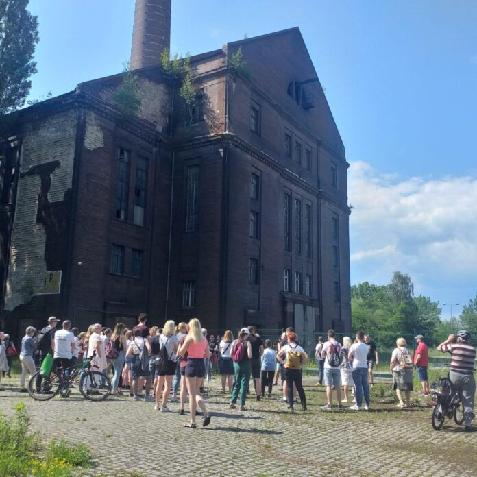 0fb72baa-afa9-4be2-84b5-994219030535 Grupa ludzi przy budynku przemysłowym