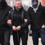 Maczety, siekiery i kokaina. Śląska policja uderzyła w brutalny gang pseudokibiców Torcidy i GieKSy Dwóch nieumundurowanych policjantów prowadzi zakutego w kajdanki mężczyznę z zakrytą twarzą; funkcjonariusze mają na rękawach opaski z napisem „Policja”