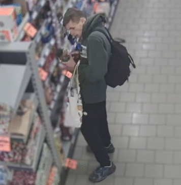 Podejrzany o kradzież na nagraniu. Rozpoznajecie go? mężczyzna w kapturze z czarnym plecakiem koło pułki sklepowej