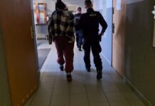 Agresywne zachowanie rodzeństwa – atak na policjantów w Świętochłowicach Zdjęcie przedstawia osobę eskortowaną przez dwóch funkcjonariuszy policji w korytarzu, najprawdopodobniej po zatrzymaniu.