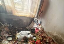 Dramat za zamkniętymi drzwiami Zaniedbane mieszkanie w Sosnowcu – łóżko i podłoga zasypane śmieciami, jedzeniem i opakowaniami, widoczne ślady wilgoci i brudu.