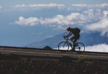 Gdzie kupić rower w Katowicach? Rowerzysta jedzie pod górę szosą na tle chmur i górskiego krajobrazu.